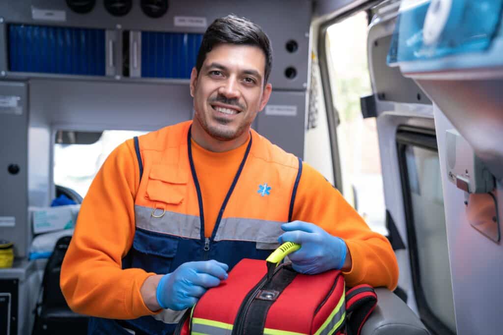 handsome young paramedic smiling inside an ambulance with a medical backpack in his hands.