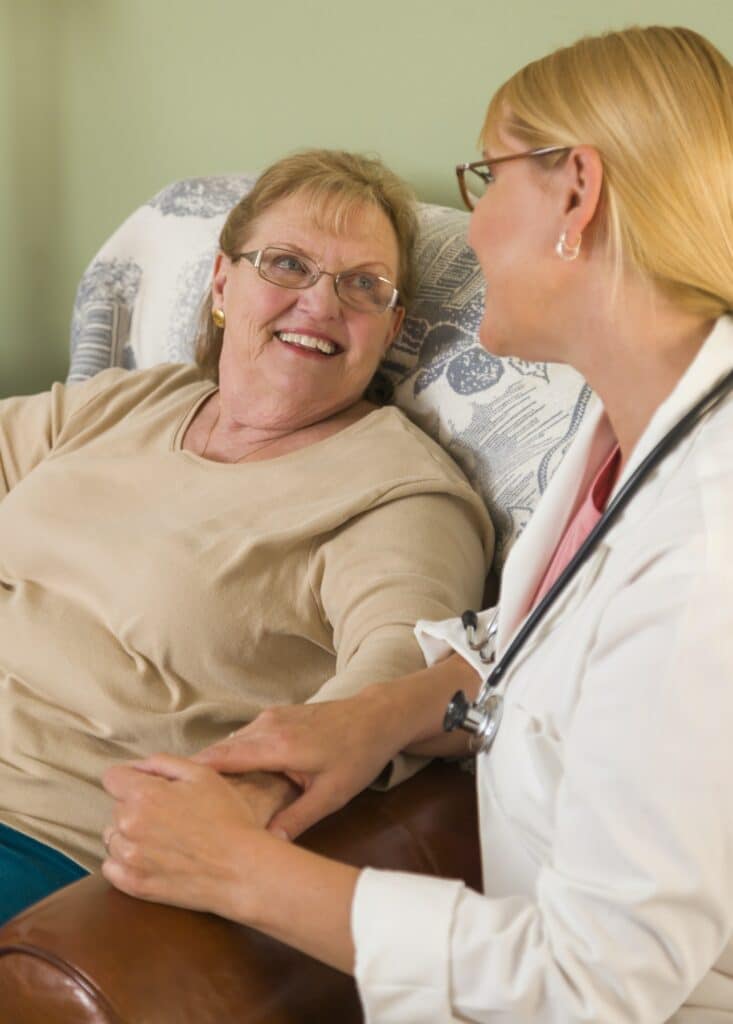 Happy Smiling Doctor or Nurse Talking to Senior Woman in Chair.